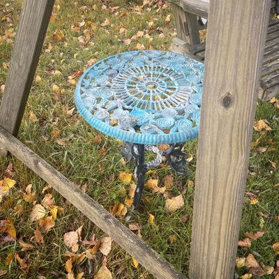 Sale Photo Thumbnail #172: Cast aluminum floral lace small patio side table with a light blue and white painted finish, positioned outdoors near a wooden structure.