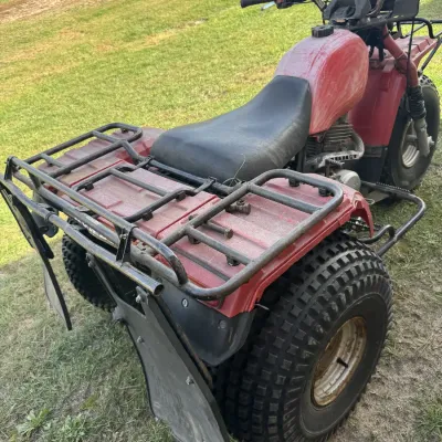 Sale Photo Thumbnail #4: Vintage red Honda Big Red three-wheeler all-terrain vehicle featuring front and rear utility racks and knobby tires.