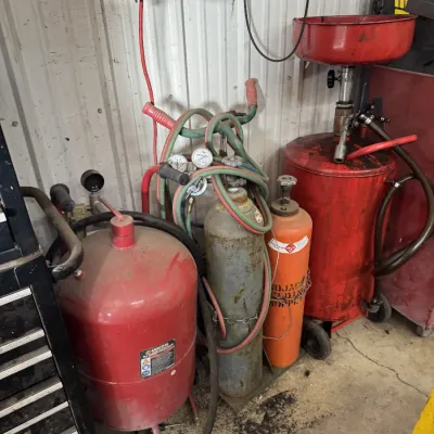 Sale Photo Thumbnail #73: Collection of workshop equipment including an oxy-acetylene welding cart with gas cylinders and regulators, a Central Pneumatic pressure abrasive blaster, and a red portable oil drain tank.