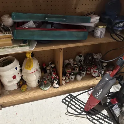 Sale Photo Thumbnail #21: Wooden shelving unit holding various collectibles, including black Americana salt and pepper shakers, ceramic cookie jars, books, and an O-Cedar spray mop in the foreground.