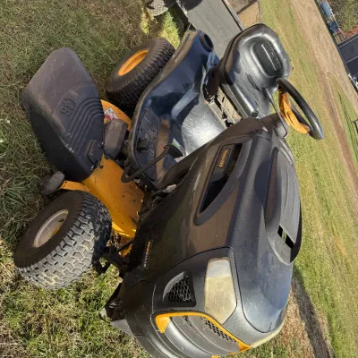 Sale Photo Thumbnail #122: Poulan Pro riding lawn mower featuring a yellow and black body with a 46-inch cutting deck, shown parked on grass near a small utility trailer.