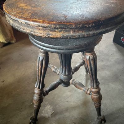 Sale Photo Thumbnail #184: Antique swivel piano stool featuring fluted wooden legs, turned stretchers, and glass ball claw feet, displaying heavy wear and age to the finish.