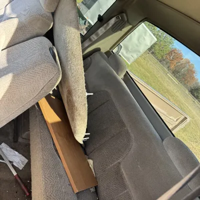 Sale Photo Thumbnail #162: Interior view of a pickup truck extended cab featuring gray cloth bench seating, loaded with loose carpet remnants and a wood panel.