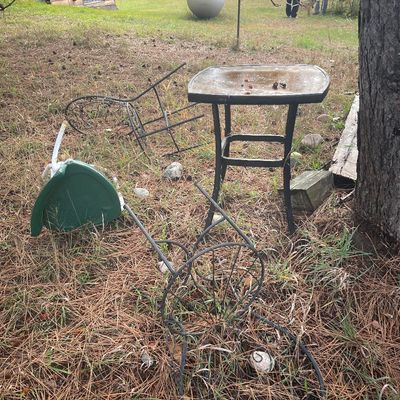 Sale Photo Thumbnail #176: Collection of outdoor patio furniture including a small black glass-top side table, wrought iron chairs, and a plastic garden seat resting in a grassy yard.