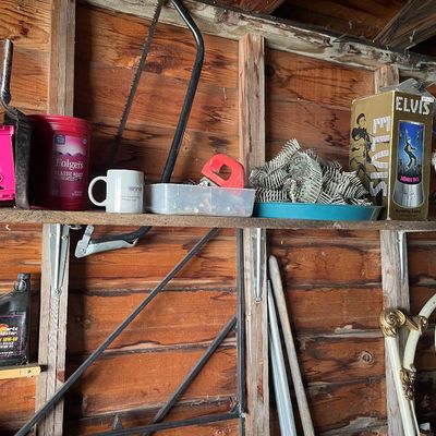 Sale Photo Thumbnail #204: Wooden garage shelving holding assorted tools, hardware, a boxed Elvis Presley rotating motion lamp, and a Folgers coffee tub.