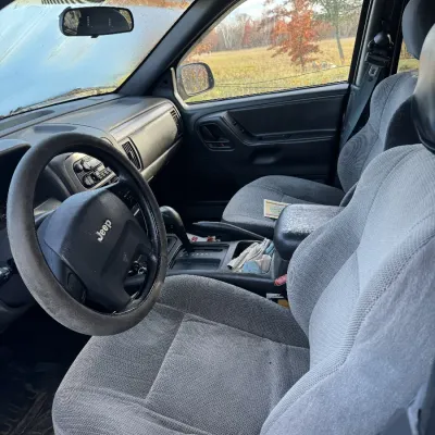 Sale Photo Thumbnail #150: Interior view of a late-1990s to early-2000s Jeep SUV featuring grey cloth seats, a steering wheel with a cover, and an automatic transmission shifter.