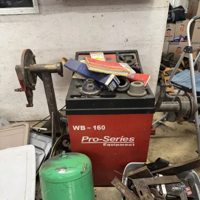 Sale Photo Thumbnail #96: Pro-Series Equipment WB-160 wheel balancer machine surrounded by various workshop tools and equipment, including a green compressed air tank.