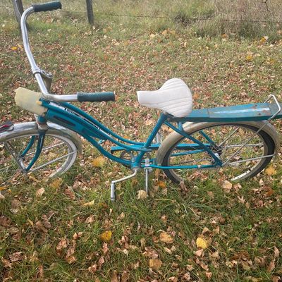 Sale Photo Thumbnail #175: Vintage teal cruiser bicycle featuring a tank headlight, rear luggage rack, white seat, and whitewall tires.