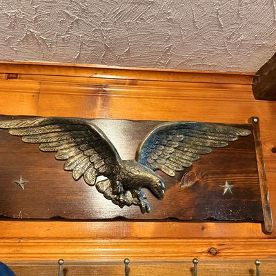 Vintage brass or cast metal American eagle wall plaque mounted on a dark wood board with star accents.