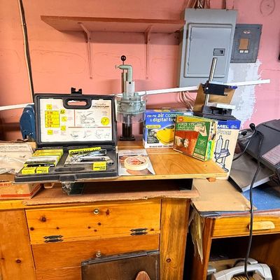 Workshop table featuring various power tools, hardware accessories, a stapler kit, drill press attachment, and a motorized sharpener or...