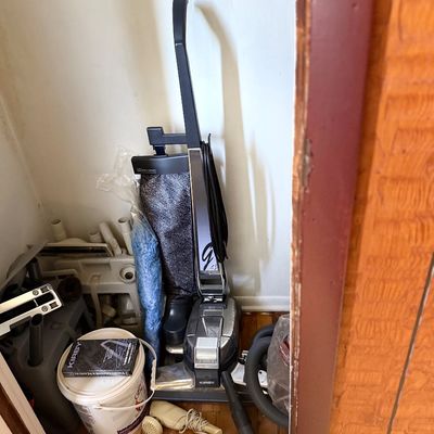 Vintage Kirby Generation 4 upright vacuum cleaner with attachments, owner's manual VHS, and caddy stored in a closet.
