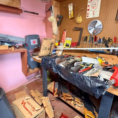 Workshop area filled with various woodworking power tools and hand tools, including a band saw, jointer, red bench vise, hand saws, and...