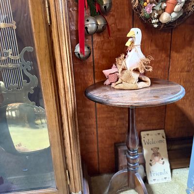 Vintage dark wood pedestal tripod side table featuring turned accents, shown alongside country-style decor items and a grandfather clock.