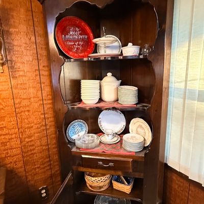 Vintage dark stain wooden corner hutch filled with various dishware, holiday plates, and serveware.