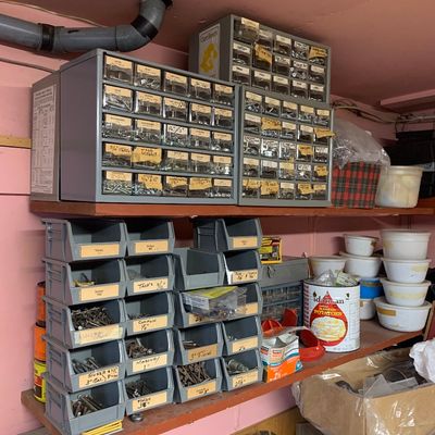 Assorted workshop hardware storage, including metal drawer organizers and stacked plastic bins filled with various screws, nails, and...
