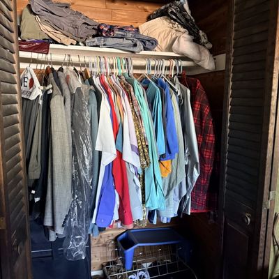 Cedar-lined closet filled with assortment of men's clothing, including shirts, jackets, and trousers, along with shoes and folded...