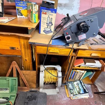 Workshop area featuring a grey tabletop power tool, a Dremel Drill Press attachment box, a cord reel with yellow extension cord, and...