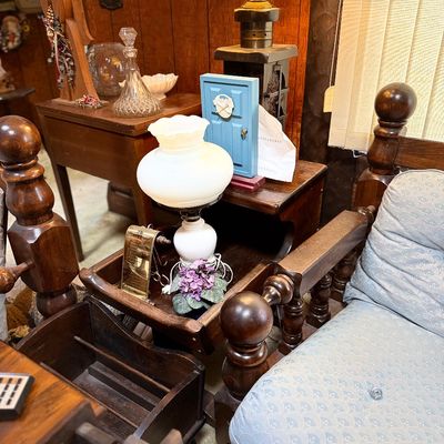 Vintage wood-frame armchair with turned finials and light blue patterned upholstery, surrounded by a rustic end table, milk glass...
