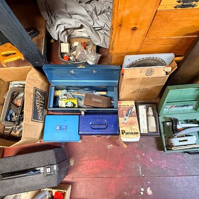 Collection of vintage tools, hard cases, and workshop equipment, including power sanders, metal toolboxes, hand saws, and C-clamps.