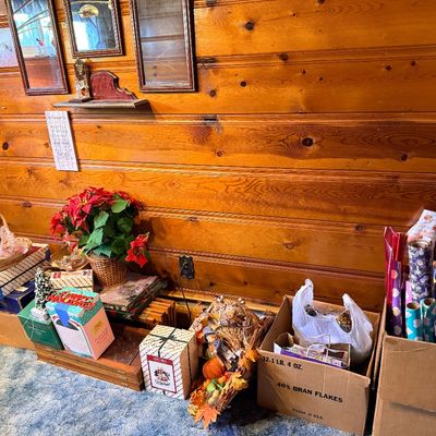 Collection of holiday decorations, gift wrapping paper, boxed decor items, and a cornucopia arranged on the floor along a wood-paneled wall.