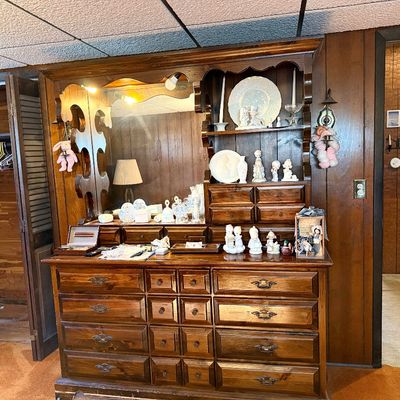 Vintage dark pine hutch dresser with attached mirror and shelving unit, decorated with decorative porcelain figurines and glassware.