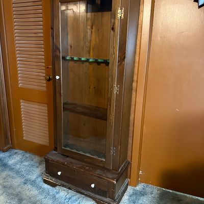 Vintage dark pine wooden gun cabinet featuring a single glass-front door, felt-lined racks, and a bottom storage drawer.