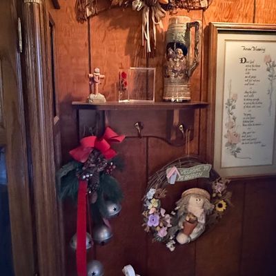 Rustic home decor display featuring a wall-mounted wooden shelf, ceramic beer stein, decorative wreaths, holiday door bells, framed...