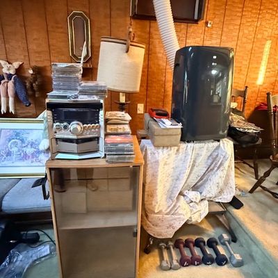 Home electronics and fitness items including a stereo system on a wooden cabinet with stacked CDs, a portable LG air conditioner unit,...