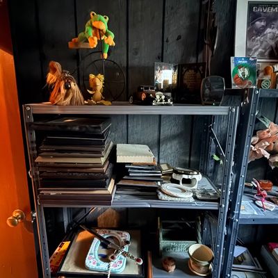 Metal shelving unit filled with eclectic collectibles, including picture frames, plush toys, maracas, framed artwork, and home decor items.