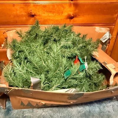 Vintage artificial Christmas tree pine branches packed inside a heavily worn, duct-taped cardboard box.