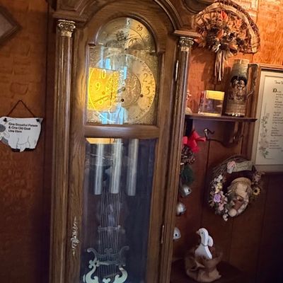 Vintage oak grandfather clock with an ornate bonnet top, brass moon phase dial, and decorative pendulum.
