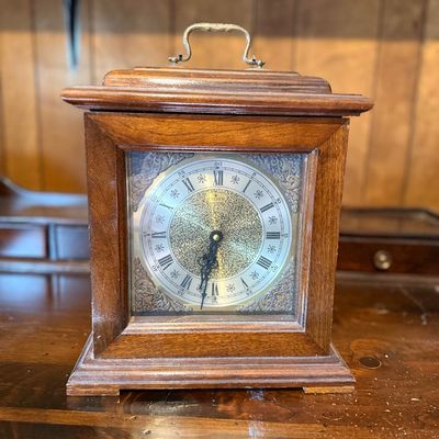 Vintage Crown bracket-style mantel clock featuring a dark wood case, brass carrying handle, and an ornate metal face with Roman numerals.