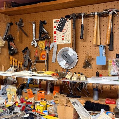 Workshop wall filled with assorted hand tools, including hammers, levels, hand planes, circular saw blades, and pegboard storage.