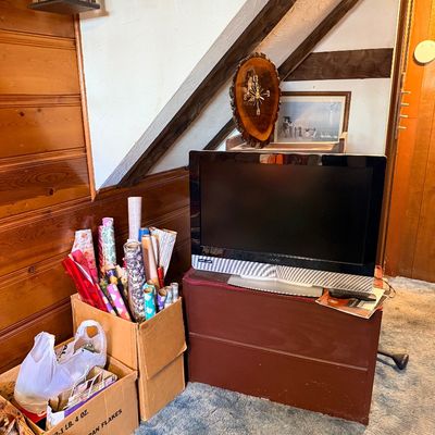 Vizio flat-screen LCD television resting on a low wooden chest, accompanied by cardboard boxes filled with wrapping paper rolls under an...