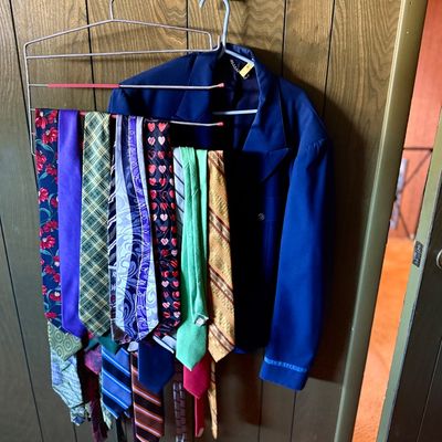 Collection of vintage neckties hanging on a multi-tier wire hanger alongside a blue jacket mounted on wood paneling.