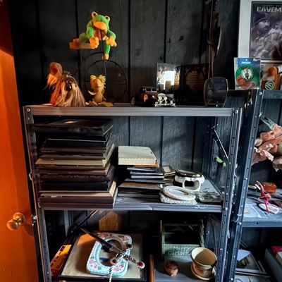 Metal shelving unit filled with miscellaneous home decor, small picture frames, plush toys, maracas, and collectibles.