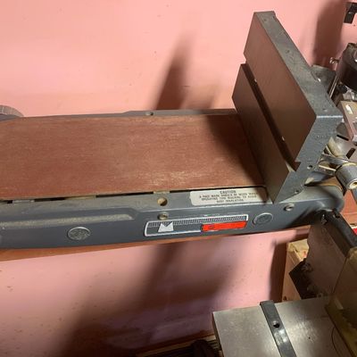 Vintage benchtop belt sander attachment featuring a cast iron frame and adjustable backstop.