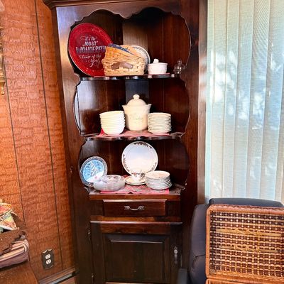 Vintage dark stained wood corner hutch cabinet with scalloped shelving frames, filled with decorative plates, bowls, and dishware.
