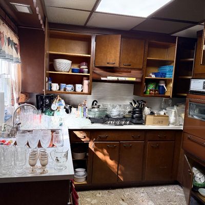 Vintage 1970s kitchen featuring dark wood cabinetry filled with glassware, kitchenware, small appliances, and a built-in wall oven.