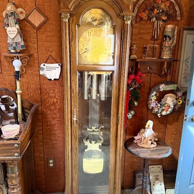 Vintage oak grandfather clock with ornate brass pendulum, moon phase dial, and glass door case.