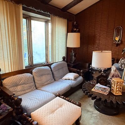 Vintage wood-frame sofa with light blue upholstered cushions, matching ottoman, and a unique gear-shaped coffee table in a wood-paneled...