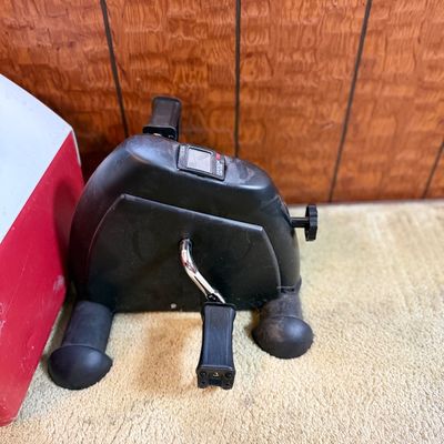 Black compact mini exercise bike pedal exerciser with digital display, showing light wear.