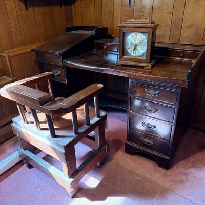 Vintage dark stain wooden desk set featuring a slanted-top side cabinet, a wooden barrel-back swivel desk chair, and a bracket-top...