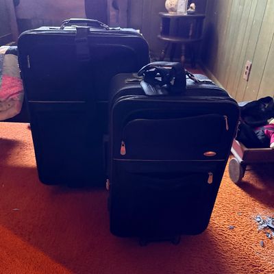Pair of modern black fabric rolling suitcases in different sizes with zippered exterior pockets.