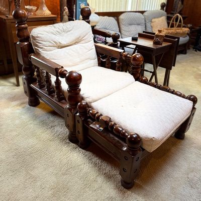 Vintage dark wood spindle-back chaise lounge with matching ottoman and cream tufted cushions.