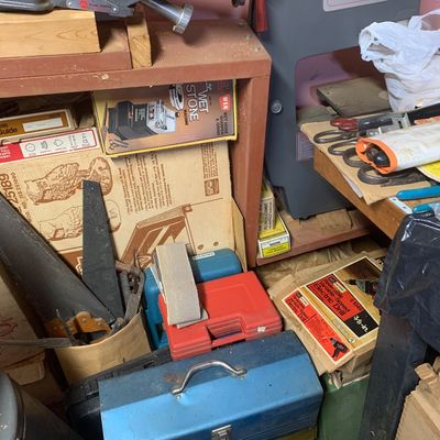 Workshop corner packed with woodworking tools, including a ShopSmith band saw, vintage hand saws, toolboxes, and boxed power tools.