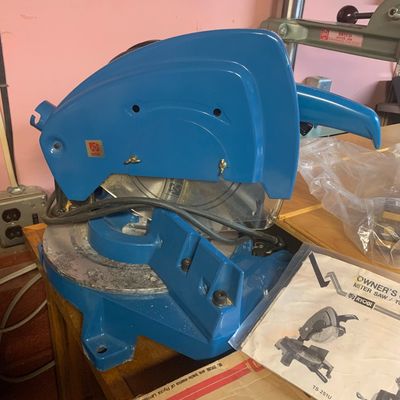 Vintage blue Ryobi TS-251U miter saw sitting on a workbench alongside its original owner's manual.