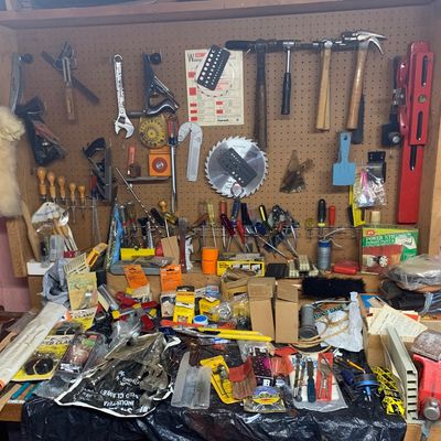 Wooden workbench and pegboard wall filled with various hand tools, hardware, clamps, and vintage shop accessories.