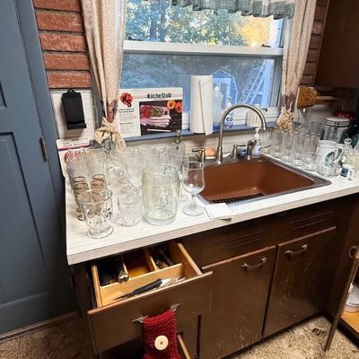 Kitchen counter area featuring an assortment of glassware, drinking glasses, and pitchers, alongside a brown sink and dark wood cabinetry.