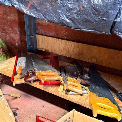 Collection of vintage hand saws and wooden hand-screw clamps stored beneath a metal workbench shelf.
